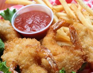 a basket of fried shrimp with fries and ketchup with a lettuce and lemon garnish
