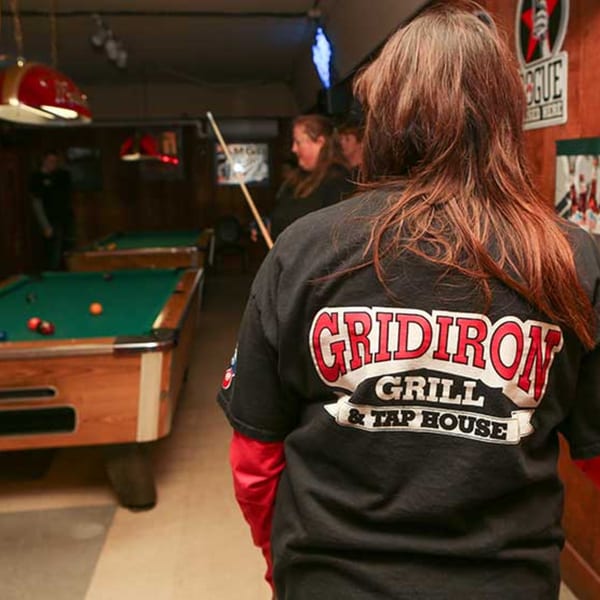 Person in a Gridiron Grill & Tap House shirt in a dimly lit pool hall.