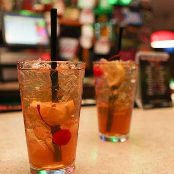 Two iced cocktails with cherries and lemon slices on a bar counter at Gridiron Grill & Tap House.