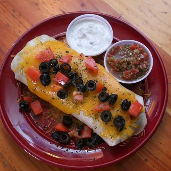 A Gridiron Grill & Tap House burrito topped with melted cheese, diced tomatoes, and black olives.