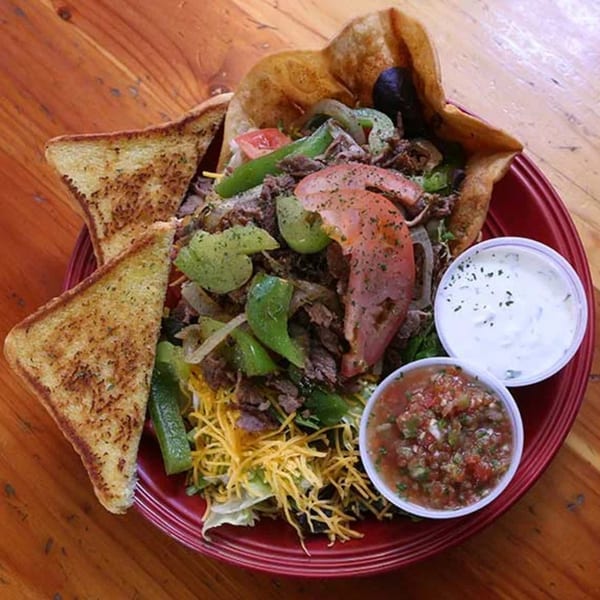 Steak taco salad in a crispy tortilla bowl with salsa, sour cream, and garlic toast.
