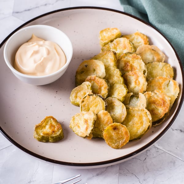 Fried pickle chips with a side of creamy dipping sauce on a light-colored plate.
