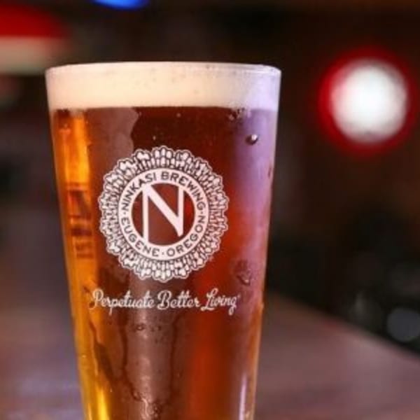 A pint glass of Ninkasi Brewing beer with a foamy head, condensation, and a dark background.